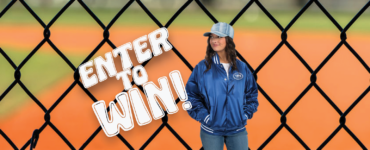 A photo of a person wearing a royal blue, satin team jacket with white strips on the cuffs, collar, and waist band, standing in front of a chain link fence. Overlaid on image are the words: Enter to Win
