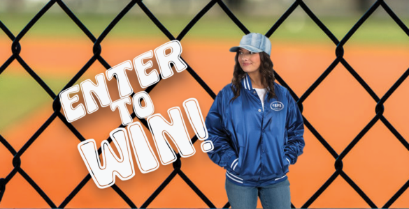 A photo of a person wearing a royal blue, satin team jacket with white strips on the cuffs, collar, and waist band, standing in front of a chain link fence. Overlaid on image are the words: Enter to Win