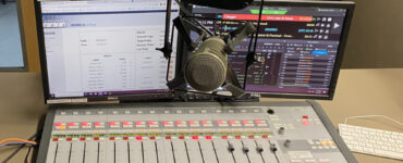 A photo of a mixing board with a microphone in front and the C89.5 logo above the microphone above