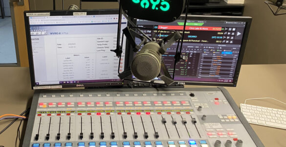 A photo of a mixing board with a microphone in front and the C89.5 logo above the microphone above
