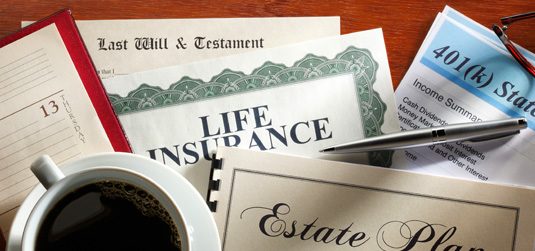 Picture of a bunch of papers on the desk. Some words visible include "Will and Testament" , "Life Insurance" and "Estate Plan"