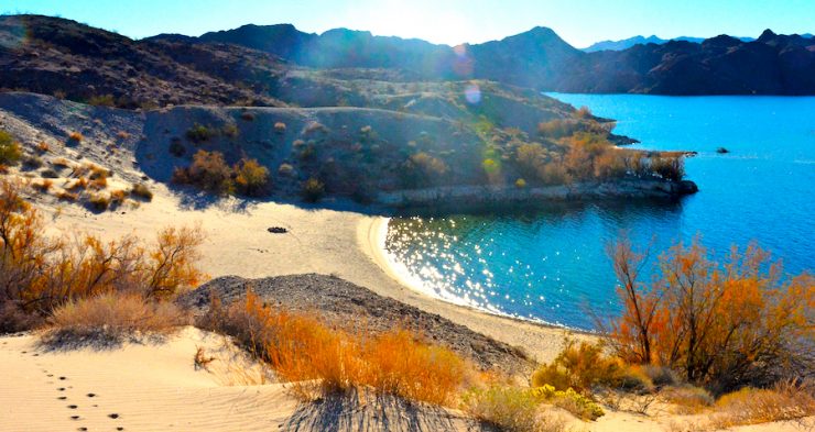 Picture of a beach on a desert lake with mountains in the background during sunset.