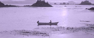 Old black and white photograph of a person in a canoe in Alaskan waters.
