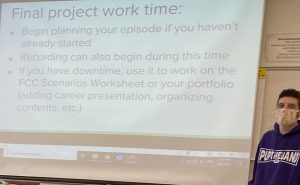 A photo of a teacher, standing in front of a projector screen with a slide labeled "Project Work Time."