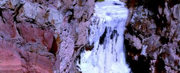 A mountain waterfall with a steep drop, fully frozen.