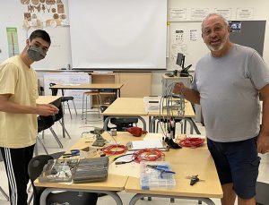 A photo of a young person with close cropped black hair and an older man with a grey beard, standing over a table of electronic components