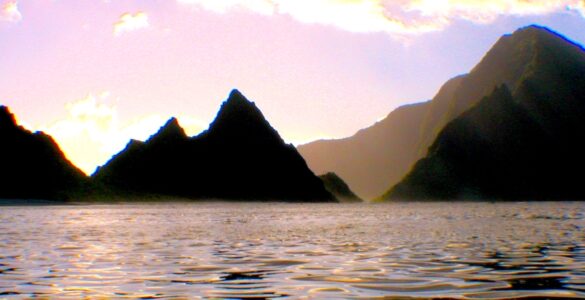 A body of water at dusk or dawn, with mountains jetting out of the water, forming islands or peninsulas. The sky is light purple and there is a light mist.