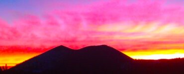 The outline of a backlit mountain. In the background is a colorful sky, illuminated by bright pink, yellow and purple clouds at sunset.
