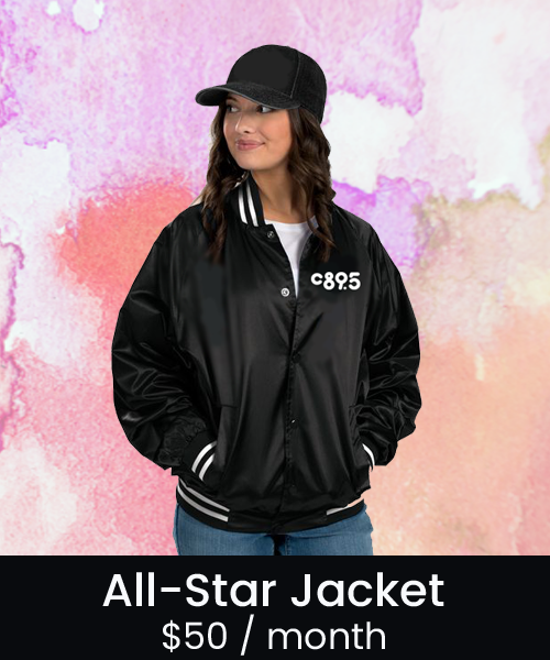 A photo of a person wearing a black, satin team jacket with white strips on the cuffs, collar, and waist band.