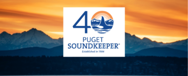 An image of an orange sunset over the Puget Sound with the number 40 with the fin of an orca in the "0" and the words "Puget SoundKeeper, established 1984"