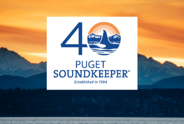 An image of an orange sunset over the Puget Sound with the number 40 with the fin of an orca in the "0" and the words "Puget SoundKeeper, established 1984"
