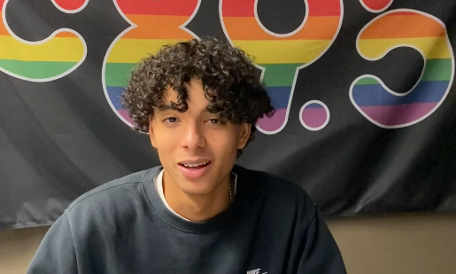 A photo of a teenage boy. He has light brown skin, brown curly hair and is smiling.