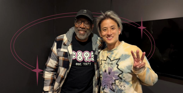 Two individuals posing for a photo in a room, one wearing a Disney-themed sweater and the other sporting a shirt with "895" printed on it.