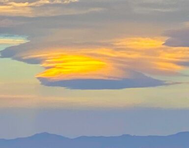A lenticular cloud shaped like a saucer, with orange and blue hues. The mountains below are faintly visible in the fading light of dusk.