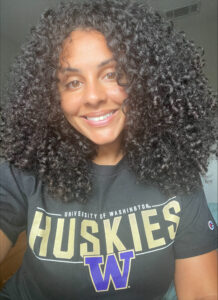 An image of a woman wearing a University of Washington t-shirt with curly black hair.