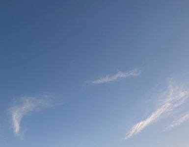 Wispy white clouds scattered across a bright blue sky on a sunny day.