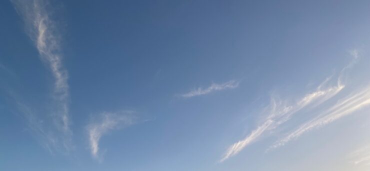 Wispy white clouds scattered across a bright blue sky on a sunny day.
