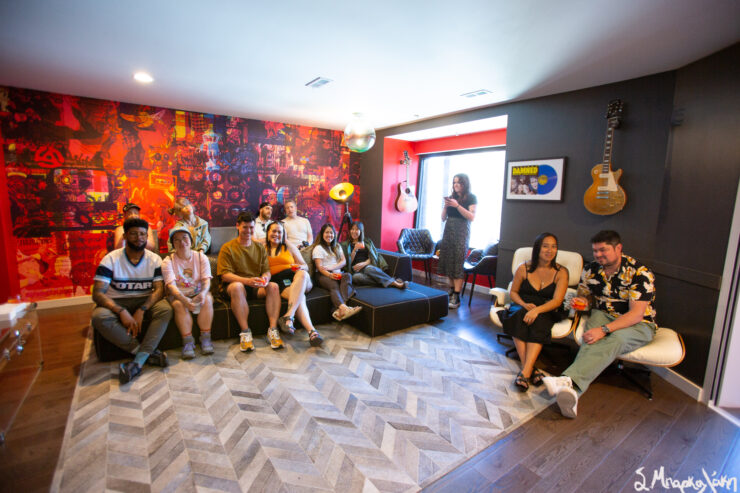 A group of people attentively watching a live music performance in a cozy room decorated with musical instruments and posters.