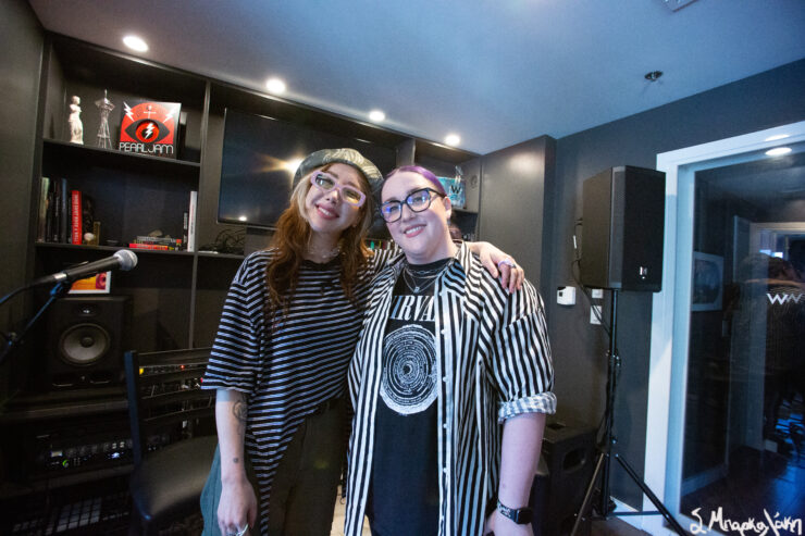 Two individuals smiling in a room, one holding an album cover with the text "Lights, Camera, Action! by Valerie Orth".