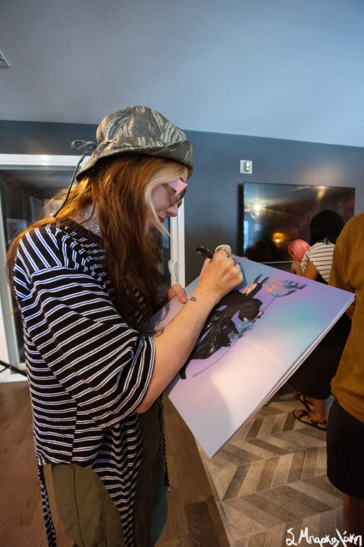 Person signing a book with illustrations at an indoor event.