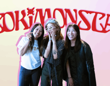 Three individuals posing with smiles in front of a neon sign that reads "TOKiMONSTA.
