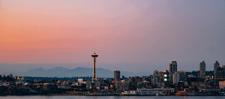 Panoramic view of Seattle skyline at sunset with the Space Needle prominently featured.