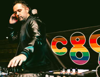DJ performing at a mixing console with a colorful "c895" logo in the background.