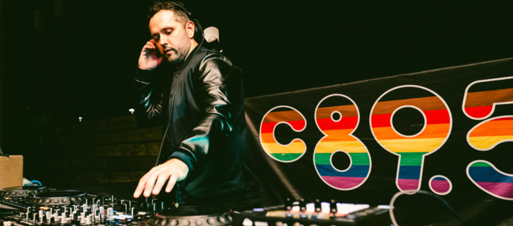 DJ performing at a mixing console with a colorful "c895" logo in the background.