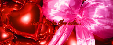 An array of shiny red heart-shaped balloons with a prominent pink bow, featuring the phrase "love is in the air..." floating amidst them.