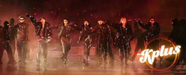 A group of performers dressed in dark clothing and sunglasses are energetically posing on stage. The image features dramatic lighting and a smoky atmosphere. The word "Kplus" is displayed in the lower right corner.