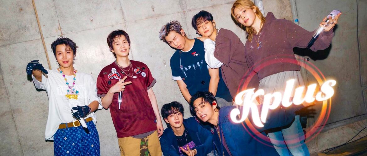 A group of seven people posing energetically in front of a concrete wall. They are dressed in stylish, casual outfits and are smiling or making playful gestures. The word "Kplus" is prominently displayed in the bottom right corner.