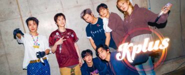 A group of seven people posing energetically in front of a concrete wall. They are dressed in stylish, casual outfits and are smiling or making playful gestures. The word "Kplus" is prominently displayed in the bottom right corner.