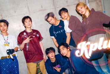 A group of seven people posing energetically in front of a concrete wall. They are dressed in stylish, casual outfits and are smiling or making playful gestures. The word "Kplus" is prominently displayed in the bottom right corner.