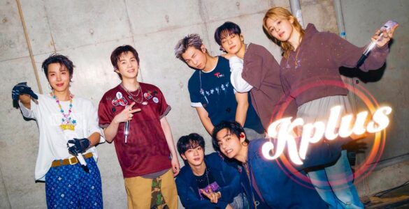 A group of seven people posing energetically in front of a concrete wall. They are dressed in stylish, casual outfits and are smiling or making playful gestures. The word "Kplus" is prominently displayed in the bottom right corner.