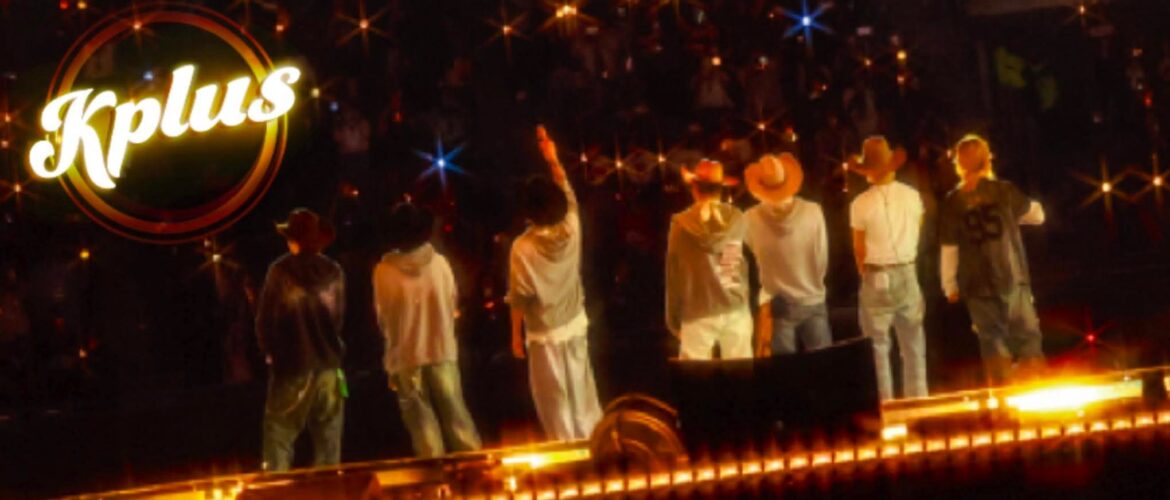 "Seven individuals stand on a stage facing an audience, with one raising a hand. They are wearing casual clothes and hats. Bright lights create a starry effect. The word 'Kplus' is visible in the upper left corner."