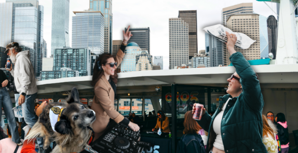 A crowded ferry deck with people taking photos and mingling, set against the backdrop of Seattle's skyline featuring tall buildings and landmarks. The top of the ferry's structure is visible, flying flags.